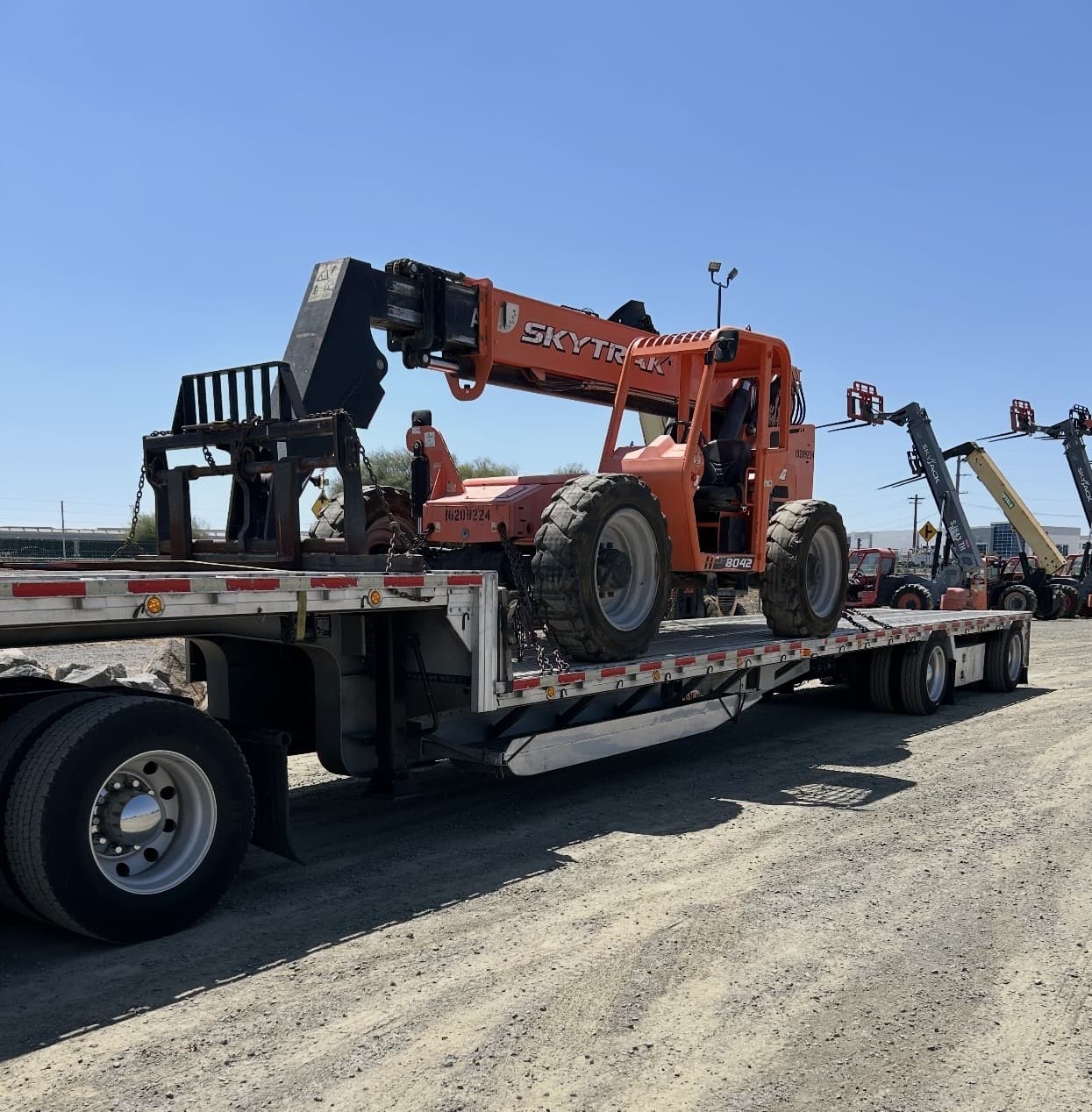 Telehandler secured on a flatbed trailer for transport.